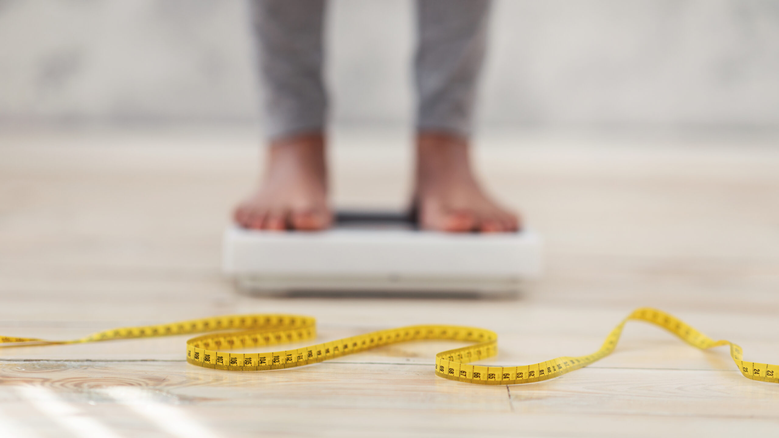 Unrecognizable Black Lady Standing On Scales, Checking Her Weight, Focus On Measuring Tape